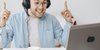 Mann mit Kopfhörern vor Laptop, der sich freut und die zeigefinger in die Luft reckt