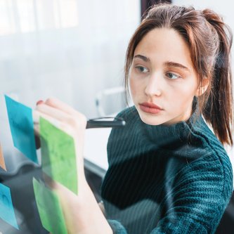 Kauffrau im Büro schreibt an Glaswand