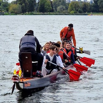 Schüler sitzen in einem Drachenboot, das auf einem breiten Fluss fährt