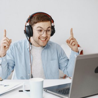 Mann mit Kopfhörern vor Laptop, der sich freut und die zeigefinger in die Luft reckt