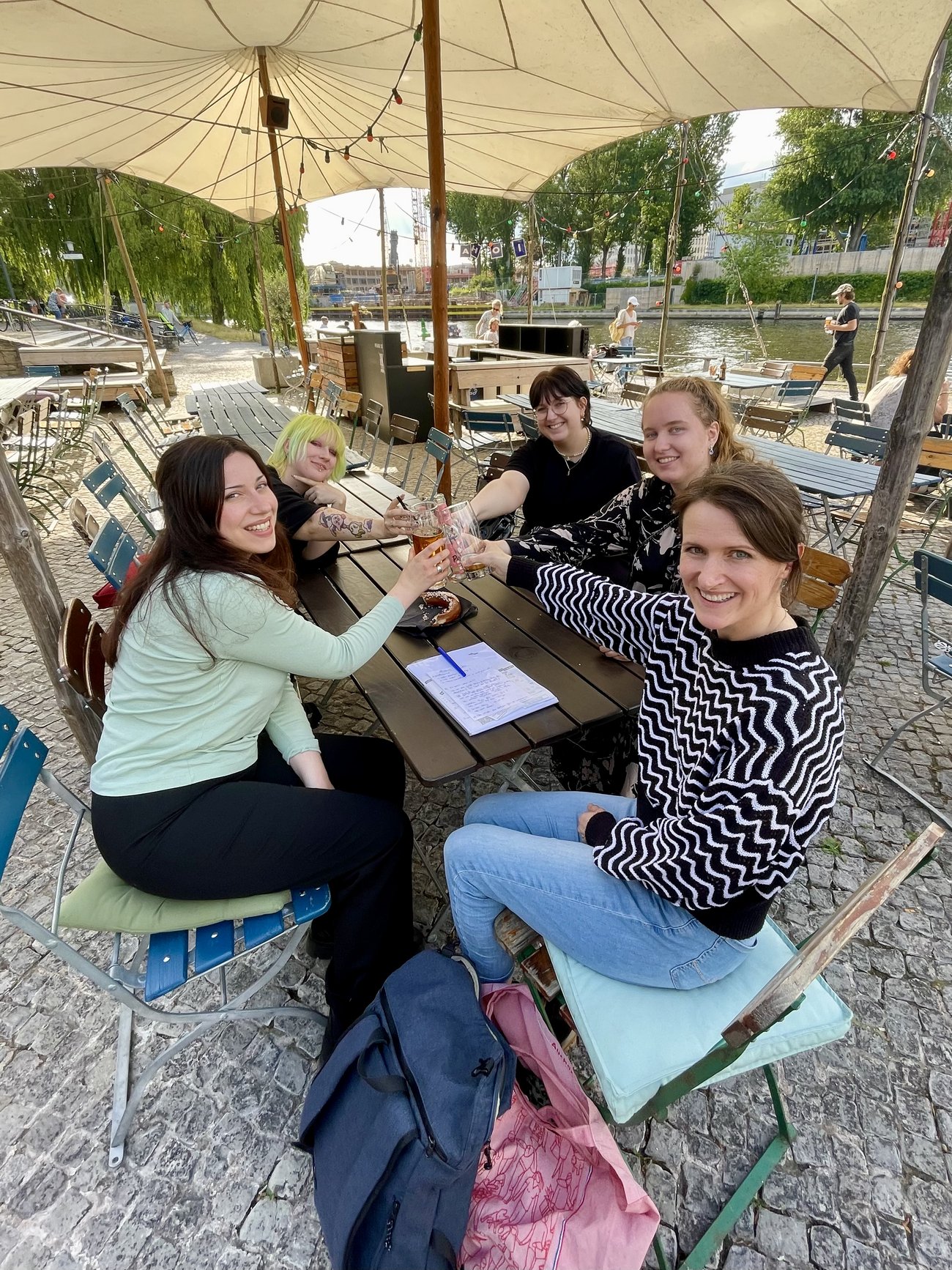 5 Frauen sitzen an einem Tisch und stoßen an