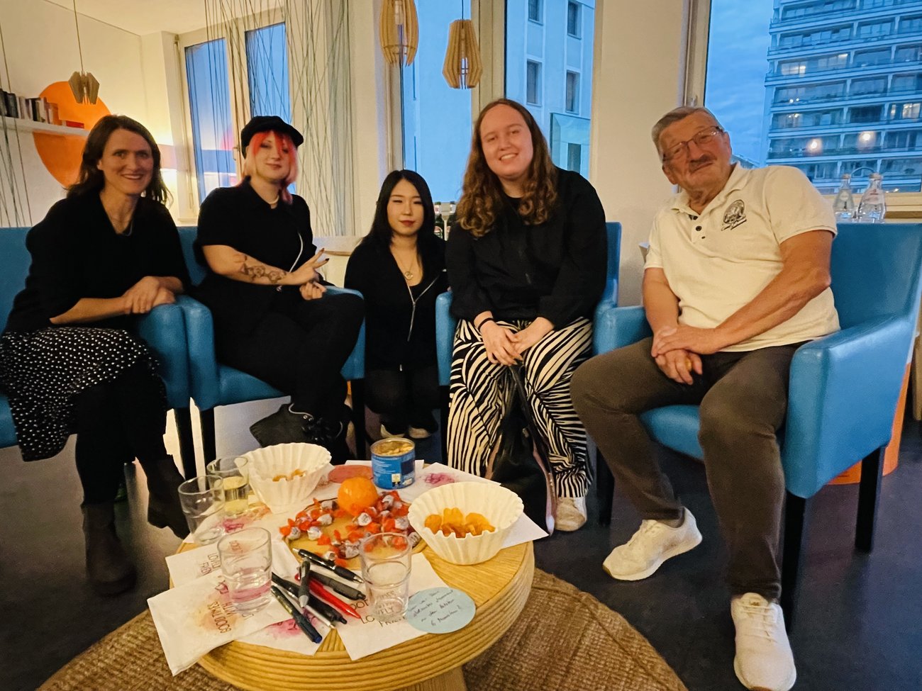 5 Personen sitzen um einen runden tisch mit Knabbereien