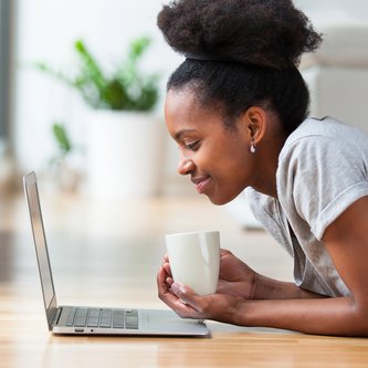 Frau entspannt liegend mit Kaffee vor dem Laptop