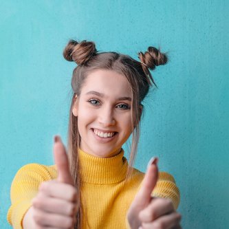 junge Frau mit gelbem Oberteil hält beide Daumen hoch