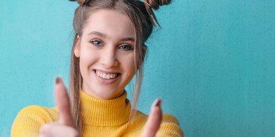 junge Frau mit gelbem Oberteil hält beide Daumen hoch
