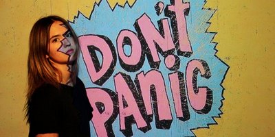 junge Frau vor Graffiti-Schriftzug "DON'T PANIC"